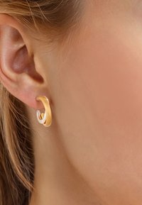 Goldene und silberne Creolen mit glatter Oberfläche, mit verschlungenen Schlaufen und polierter Textur, getragen an einem Ohr.