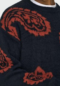 Marine gebreide sweater met grote rode bloemenpatronen, met een harige textuur en geribbelde ronde hals. Geen zichtbare sluitingen of zakken.
