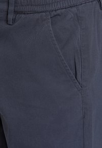 Granatowe, lekkie spodnie z tkaniny o gładkiej fakturze i boczną kieszenią. Posiadają elastyczny pas dla wygody.