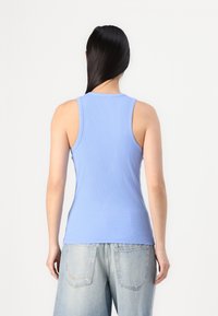 Svjetloplava rebrasta majica bez rukava s okruglim izrezom i uskim naramenicama, u kombinaciji s širokim svjetloplavim traper šortsevima.