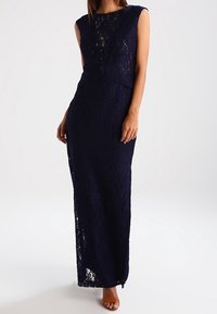Robe maxi en dentelle bleu marine avec un motif floral, sans manches, au design ajusté, dotée d'un décolleté en V profond et d'un dos ouvert.