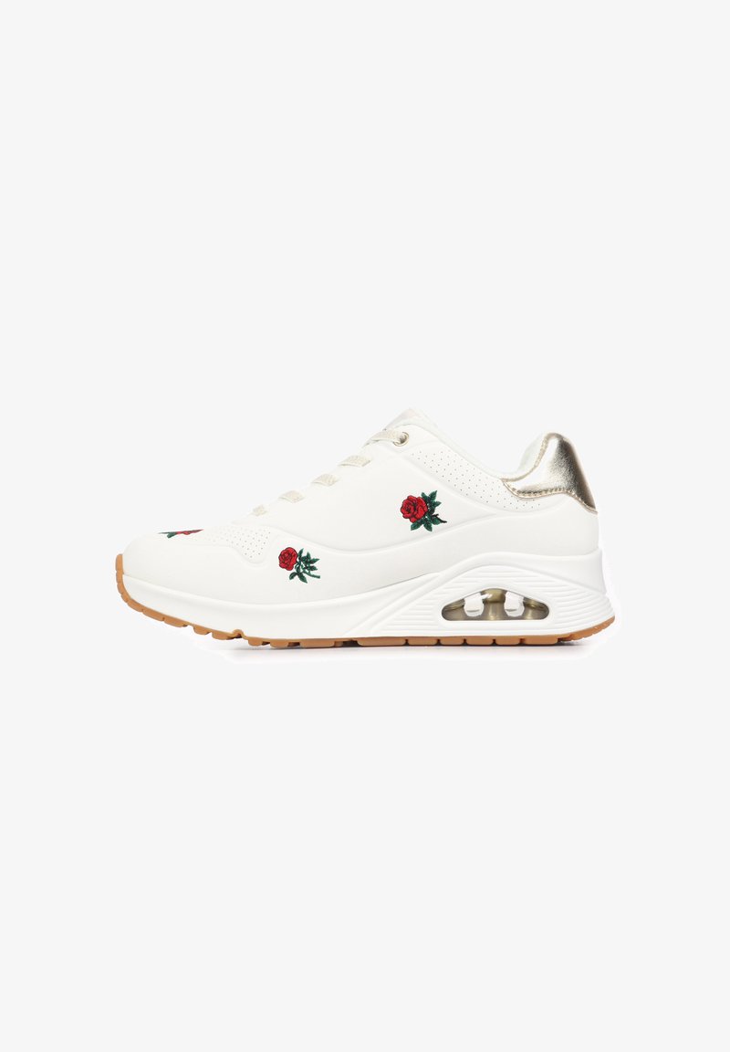 Λευκό αθλητικό παπούτσι με κεντήματα κόκκινης τριανταφυλλιάς, χρυσή λεπτομέρεια στη φτέρνα και ορατό αερόσακο στη σόλα πάνω σε ανοιχτό καφέ πέλμα.