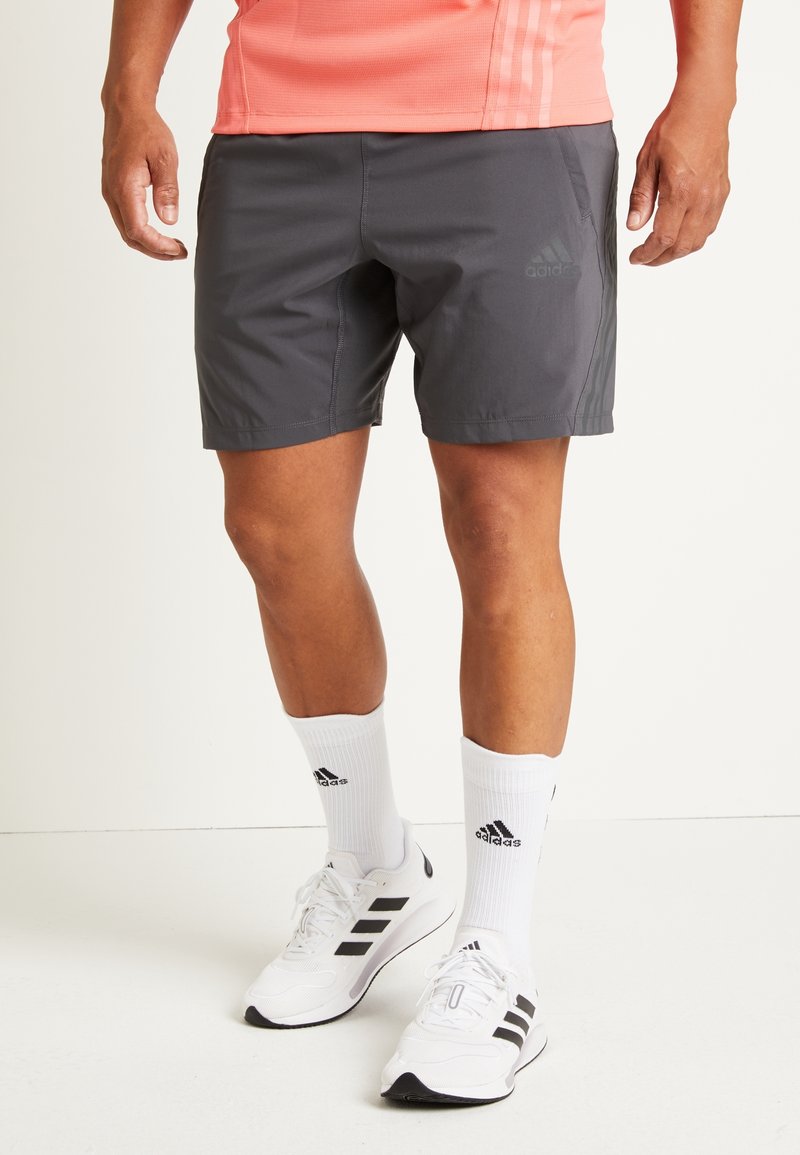Harmaat urheilushortsit, jotka on valmistettu kevyestä materiaalista, elastisella vyötärönauha ja tummanharmaa Adidas-logo. Yhdistä valkoisten sukkien ja kenkien kanssa.