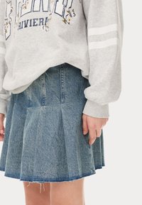 Sweatshirt gris avec broderie florale et rayures blanches, associé à une jupe plissée en jean avec un ourlet effiloché.