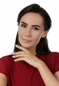 Anello con diamante rotondo e incastonatura quadrata, realizzato in metallo bianco. Il modello indossa un top rosso, mostrando unghie curate e un'espressione neutra.