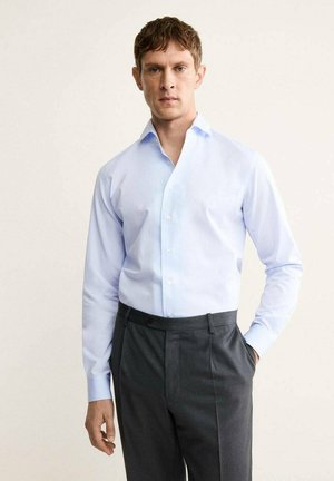 Camicia a maniche lunghe di un blu chiaro con colletto a punta, davanti con bottoni e una consistenza liscia, abbinata a pantaloni grigi scuri su misura.