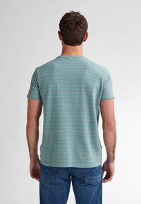 T-shirt à manches courtes et col rond en teal avec de fines rayures beiges. Texture douce, coupe décontractée et ourlet droit, associé à un jean bleu.