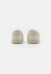 Un paio di sneaker casual beige e bianche viste da dietro su uno sfondo bianco uniforme.