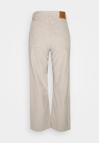 Beige corduroy wijde pijpen broek met een hoge taille, twee achterzakken en een textuurafwerking. Gemarkeerd met een bruine leren merkpatch aan de achterkant.