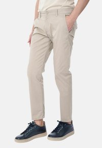 Chino beige in cotone con vestibilità rilassata, dotati di tasche laterali, passanti per cintura e una linea frontale piatta. Abbinati a sneakers blu navy.