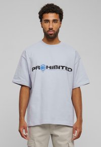 Lichtgrijze oversized t-shirt met korte mouwen, met "PROHIBITED" in vetgedrukte zwarte letters en een blauw wereldbolontwerp.
