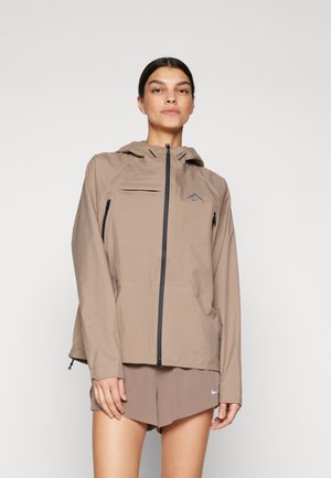 Lightweight beige jacket with a hood, featuring a zip front, one chest pocket, and logo detail. Smooth texture and relaxed fit.