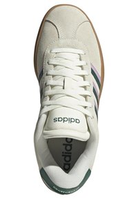 Adidas sneakers featuring a cream suede upper, three green and pink stripes, white laces, and a rubber sole with branding on the tongue.