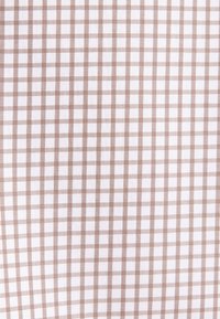 Tessuto di cotone con un motivo a quadretti marrone e bianco. I quadrati sono distribuiti uniformemente, conferendo un aspetto strutturato e geometrico.