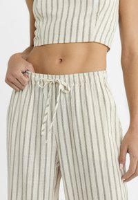 Haut court en mélange de lin et pantalon à jambes larges rayé, crème avec des rayures foncées. Comprend une taille élastique et un détail de cordon de serrage.