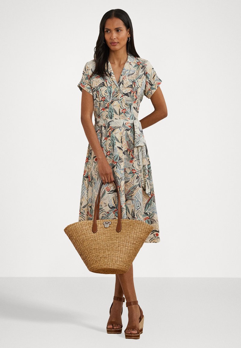 Sukienka w kwiatowy wzór z krótkimi rękawami, dekoltem w kształcie litery V, paskiem w talii i pełną spódnicą. Zestawiona z plecioną torbą ze słomy i brązowymi sandałami na obcasie.
