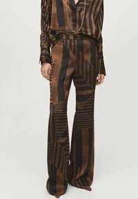 Hnedo-čierny vzorovaný outfit s dlhým rukávom a rozšírenými nohavicami. Materiál je hladký s geometrickými vzormi a pruhmi.
