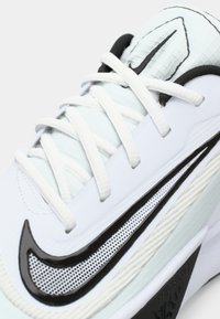Nærbillede af en hvid sneakers med hvide snørebånd, et sort- og hvidt Nike swoosh, samt teksturerede detaljer på tungen og sidepanelet.