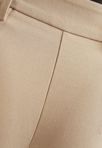 Beige kalhoty na míru s hladkým textilním povrchem, s čistým švem na přední straně a strukturovaným pasem.