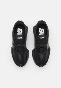 Zapatillas deportivas negras de malla y ante, con una suela de goma gruesa, cordones redondos y un logotipo prominente en la lengüeta.