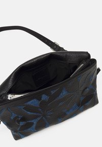 Schwarze Lederhandtasche mit blauen Denim-Akzenten und geprägtem Blumendesign. Verfügt über einen offenen Oberteil und ein Innenfach mit Reißverschluss. Verstellbarer Tragegurt enthalten.