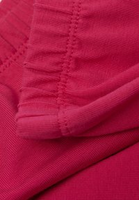Tissu rose vif avec une surface texturée, ornée de volants élastiques et de coutures nettes, démontrant une élasticité et une finition lisse.