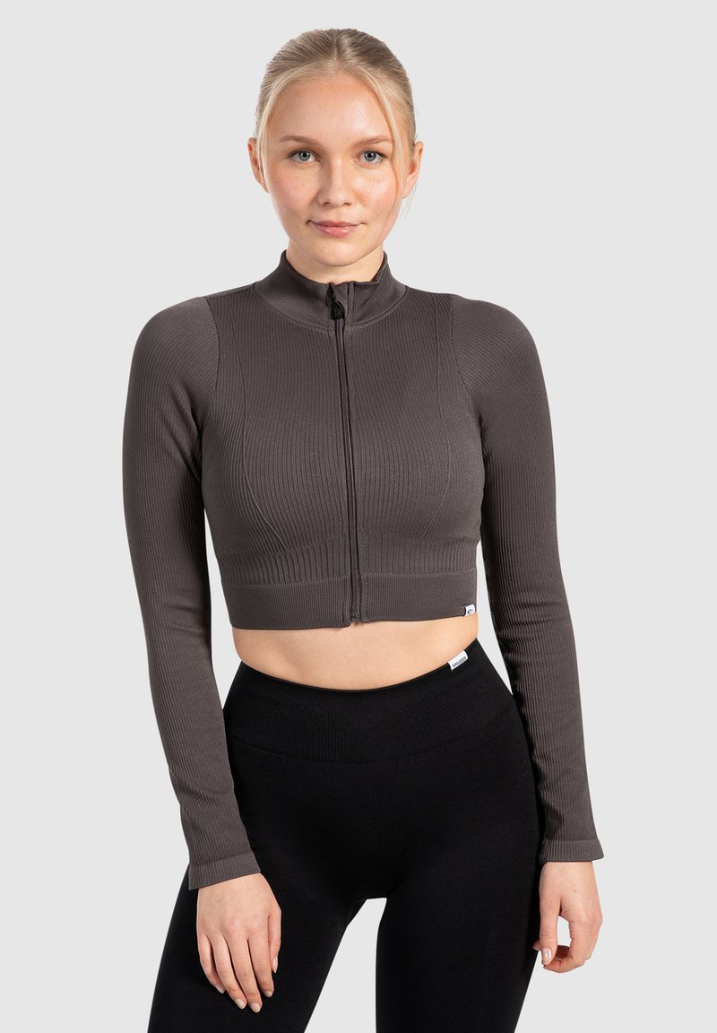 Brauner gerippter, kürzerer Reißverschluss-Oberteil mit langen Ärmeln und hohem Kragen; kombiniert mit schwarzen, hochgeschnittenen Leggings mit glatter Textur.