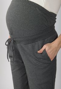Pelēki grūtniecības bikses ar elastīgu jostasvīru, aukliņu detaļu un sānu kabatām. Mīksts, elastīgs audums pielāgojas augošai vēderam.