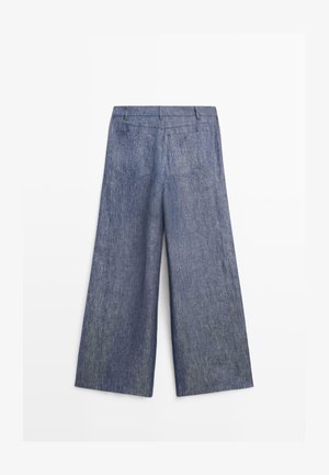 Blå denimbukser med vide ben, set bagfra med bæltestropper og to baglommer med lapper.