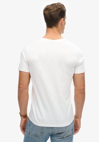 Biała krótka koszulka z krótkim rękawem, okrągłym dekoltem i gładką fakturą, z delikatnym wzorem melanżowym i luźnym krojem.