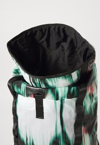 Sac à dos à rabat avec un imprimé abstrait vert vif et noir. L'intérieur est doublé d'un noir lisse. Équipé de poignées et de matériel noir robustes.