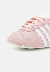 Zapatilla de ante rosa claro con rayas y costuras blancas, puntera redondeada y suela texturizada. Los cordones combinan con el color del zapato.