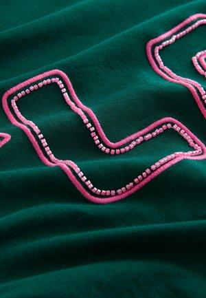 Green fabric with pink embroidery forming a wavy pattern. The texture appears soft, highlighting raised stitched details and shiny elements.