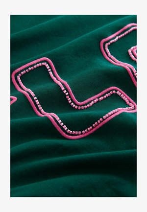 Green fabric with pink embroidery forming a wavy pattern. The texture appears soft, highlighting raised stitched details and shiny elements.