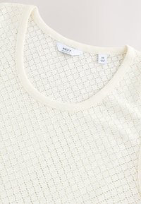 Top in maglia color crema chiaro con motivo geometrico, scollo a giro e bordatura a costine. Etichette indicano la taglia M e il marchio NEXT.