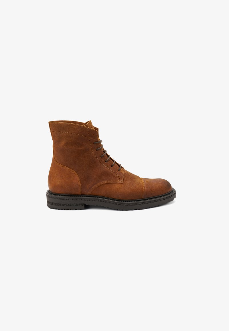 Stivaletti alla caviglia in suede marrone con punta rotonda, lacci frontali e suola in gomma robusta. Presentano dettagli con pannellature e cuciture rinforzate.
