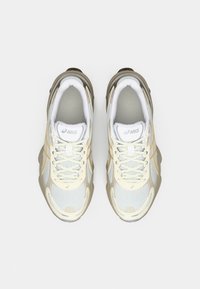 Ett par beige och vita ASICS löparskor sedd uppifrån på en helt vit bakgrund.