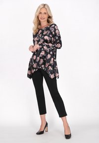 Sort blomstret langærmet top med lyserøde og hvide blomster, asymmetrisk kant, parret med sorte slim pants og sorte hæle.