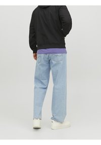 Jasnoniebieskie jeansy denim o luźnym kroju, jasnym wypraniu i subtelnych detalach przeszyć. Połączone z fioletowym t-shirtem i czarną bluzą z kapturem.
