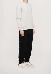 Felpa in pile grigia chiara con colletto a girocollo e polsini a coste, abbinata a jeans neri e sneakers bianche con dettagli neri.