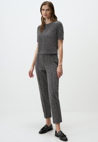 Maglietta grigia a maniche corte con texture abbinata a pantaloni a vita alta dello stesso colore. Mocassini neri con dettaglio a fiocco completano l'outfit.