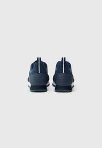 Navy blue athletic shoes with a smooth upper, textured rubber sole, and heel pull-tab. Features embossed logo detail on the heels.