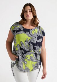 Top de patrón azul marino y verde lima con diseño de cachemira en tela suave, escote redondo y mangas cortas, combinado con pantalones blancos.