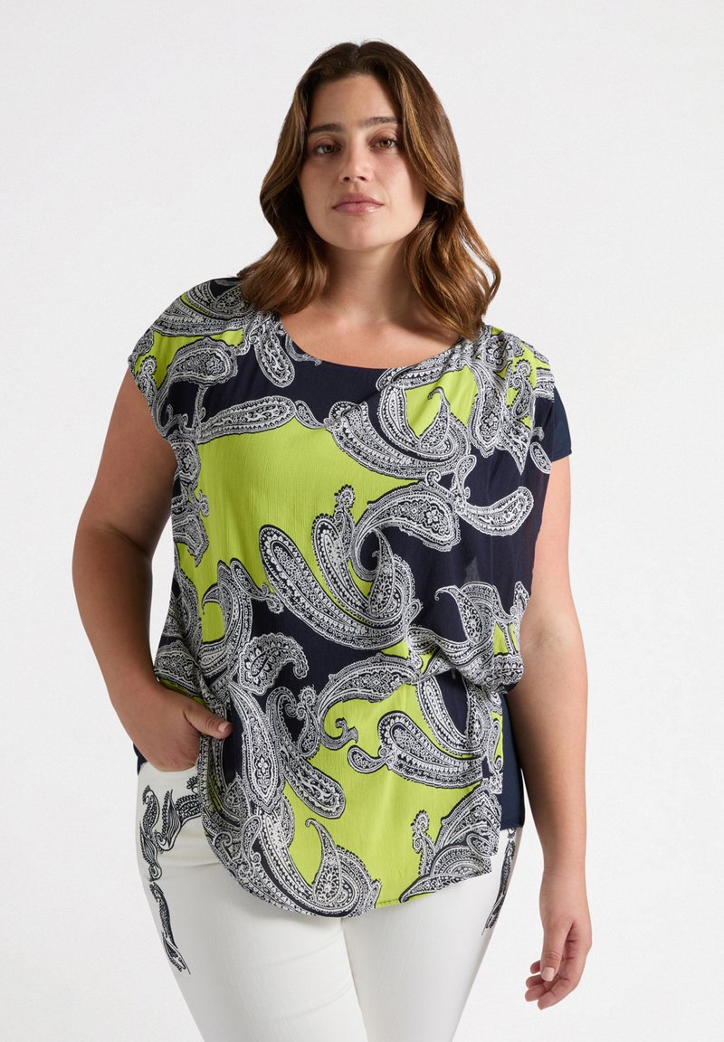 Top de patrón azul marino y verde lima con diseño de cachemira en tela suave, escote redondo y mangas cortas, combinado con pantalones blancos.