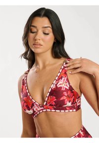 Kwiatowy biustonosz w głębokim czerwonym kolorze z różowymi i białymi kwiatami. Charakteryzuje się głębokim dekoltem w kształcie V oraz dekoracyjnym przeszyciem wzdłuż brzegów.