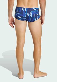 Niebieskie kąpielówki z wirującym wzorem w jaśniejszych odcieniach, materiał ma gładką teksturę, a krój zapewnia dopasowane dopasowanie.