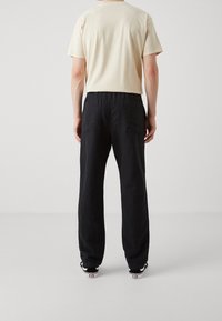 T-shirt en coton beige à manches courtes, assorti d'un pantalon ample en lin noir avec deux poches arrière. Design simple, sans motifs apparents.