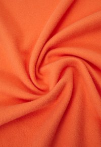 Tejido de forro polar suave color naranja con una textura lisa, presentando visualmente pliegues y un patrón en espiral, enfatizando su calidez y flexibilidad.