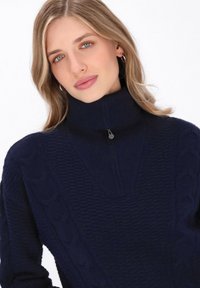 Dunkelblaues Strickpullover mit hohem Kragen und halbem Reißverschluss. Verfügt über strukturierte Muster und Zopfmuster-Elemente. Weiches, warmes Material.