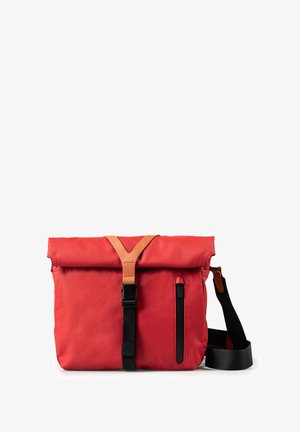 Red fabric messenger bag with a rolled top, leather strap, and black zipper pocket. Adjustable strap, rectangular shape, smooth texture.